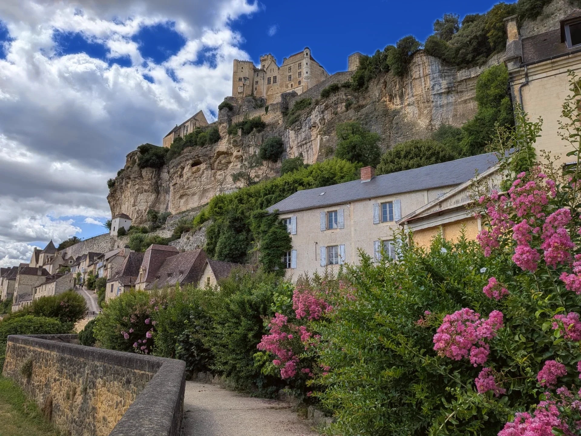 Pink summer blossom framing the village houses and Château de Beynac above