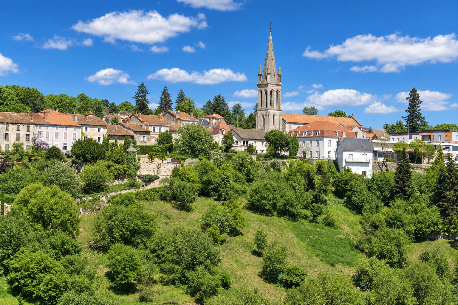 The church spire rises above houses on the hillside in Nontron, with gardens and trees below.