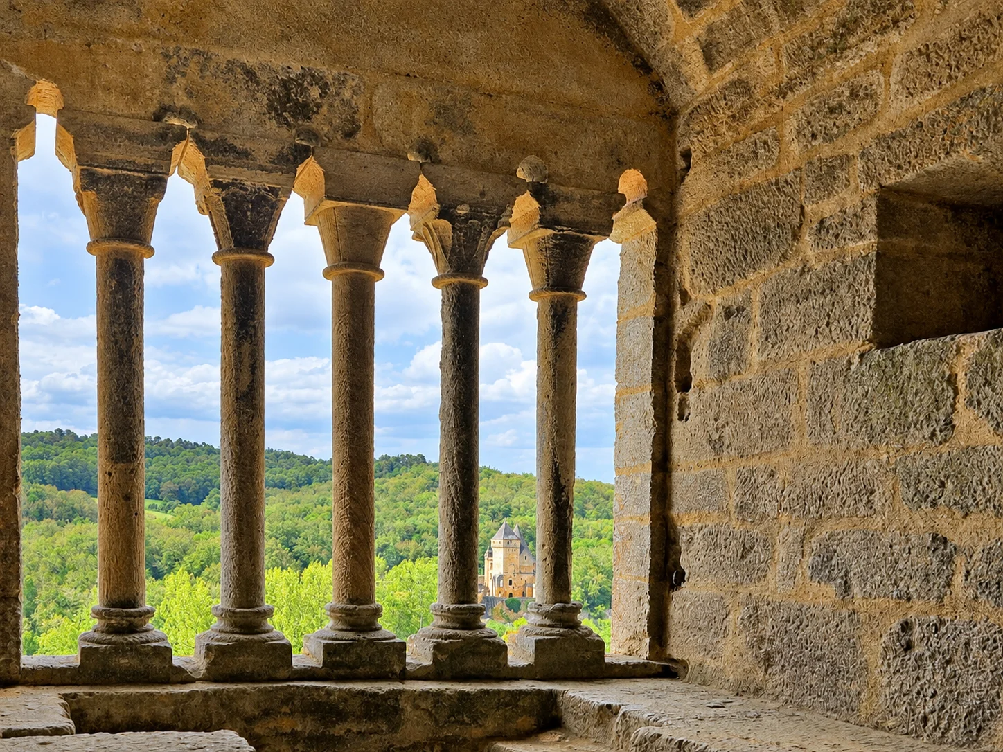 A columned window inside Château de Commarque overlooks woodland and a neighbouring château.