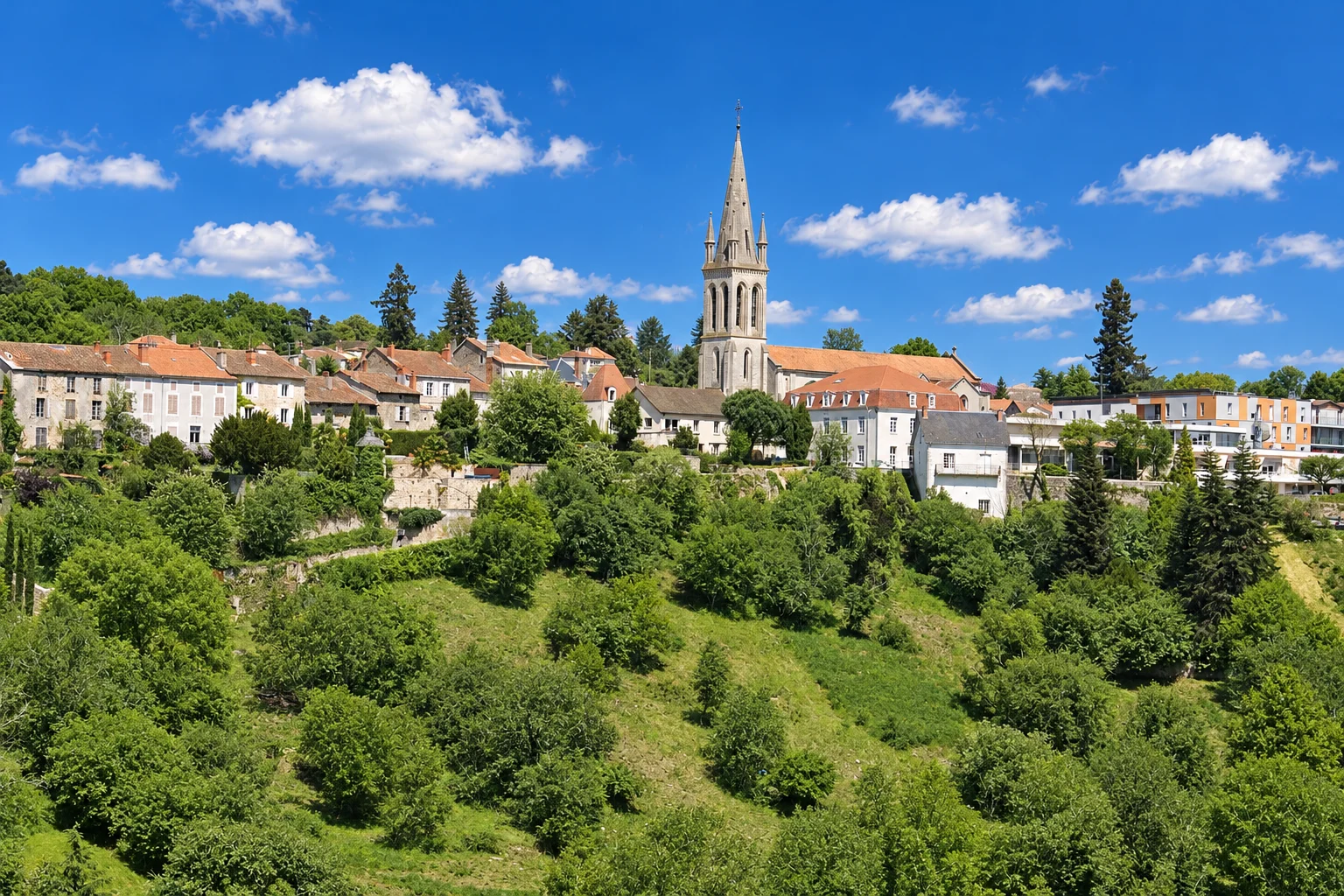 A church spire rises above the houses of Nontron and the wooded hillside below.
