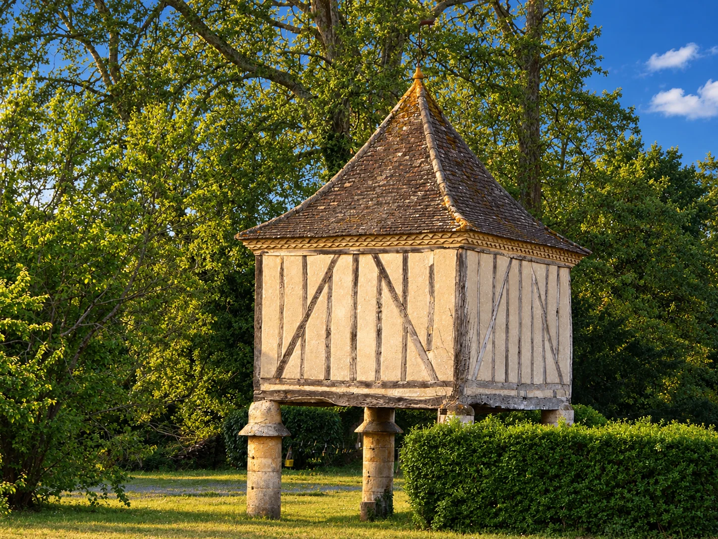 A half-timbered dovecote stands on stone pillars among trees at Lalinde.