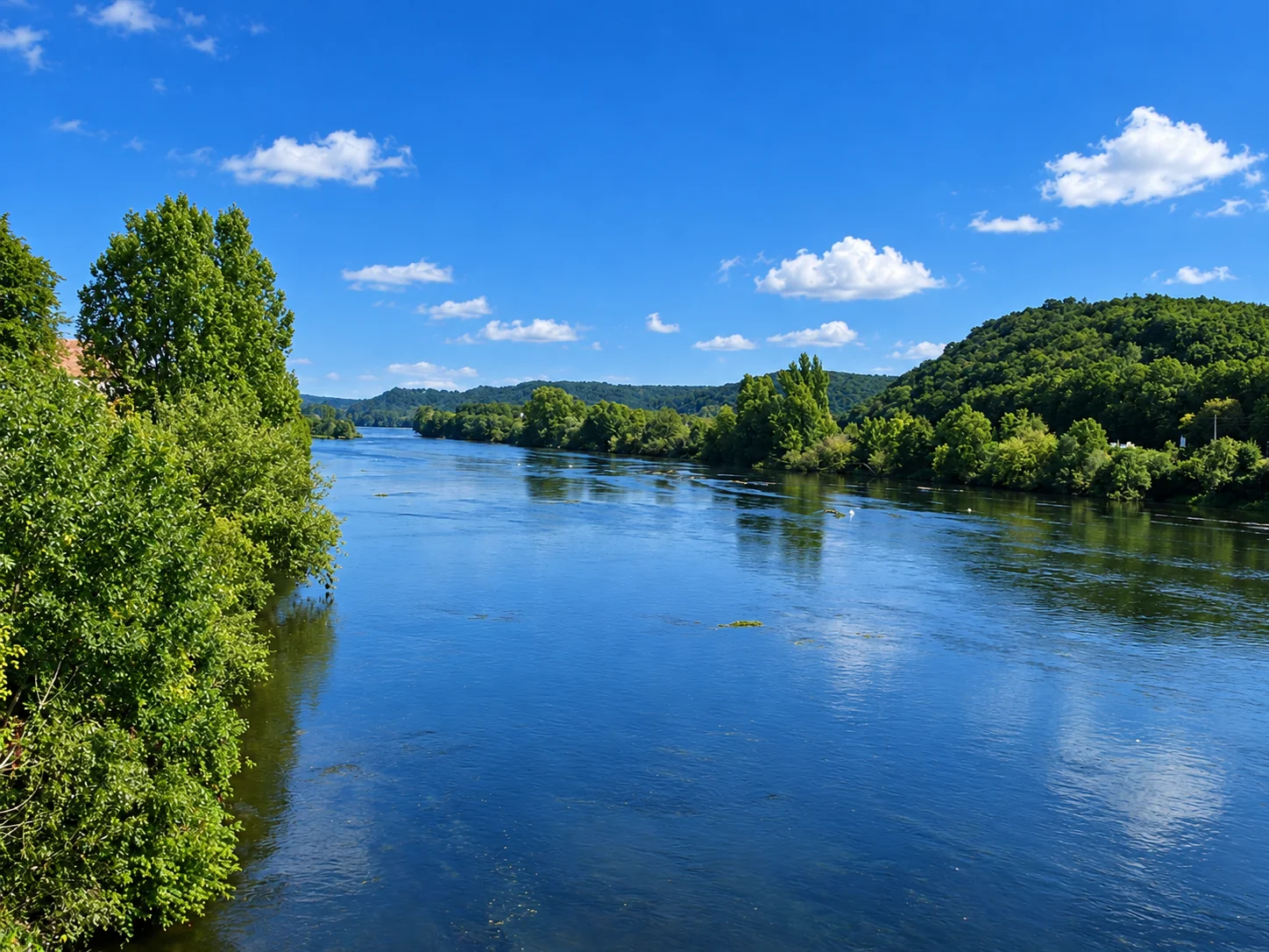 The Dordogne flows between tree-lined banks and wooded hills at Lalinde.