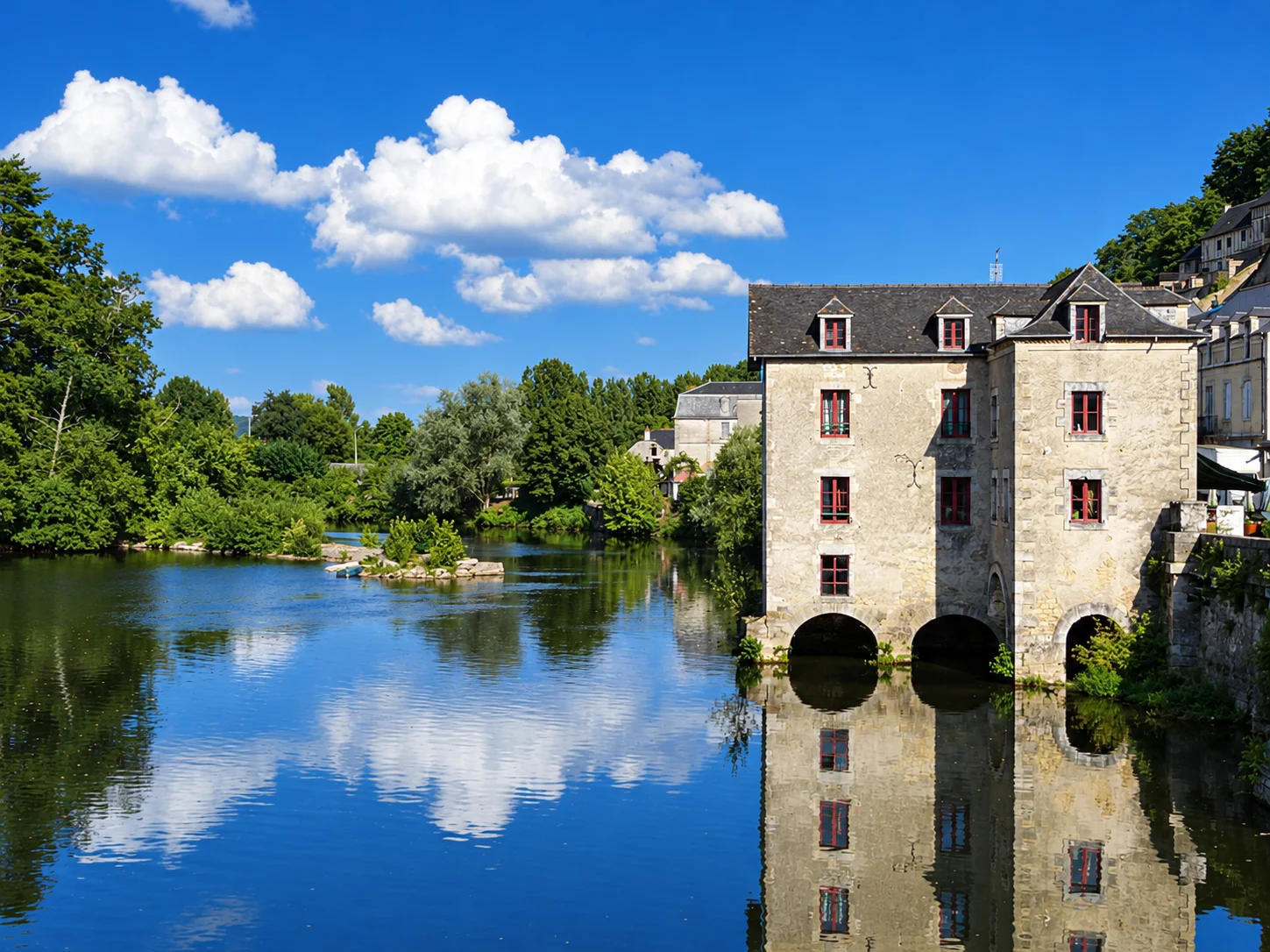 Terrasson's old mill and riverside trees are reflected in the Vézère beneath a cloud-filled sky.
