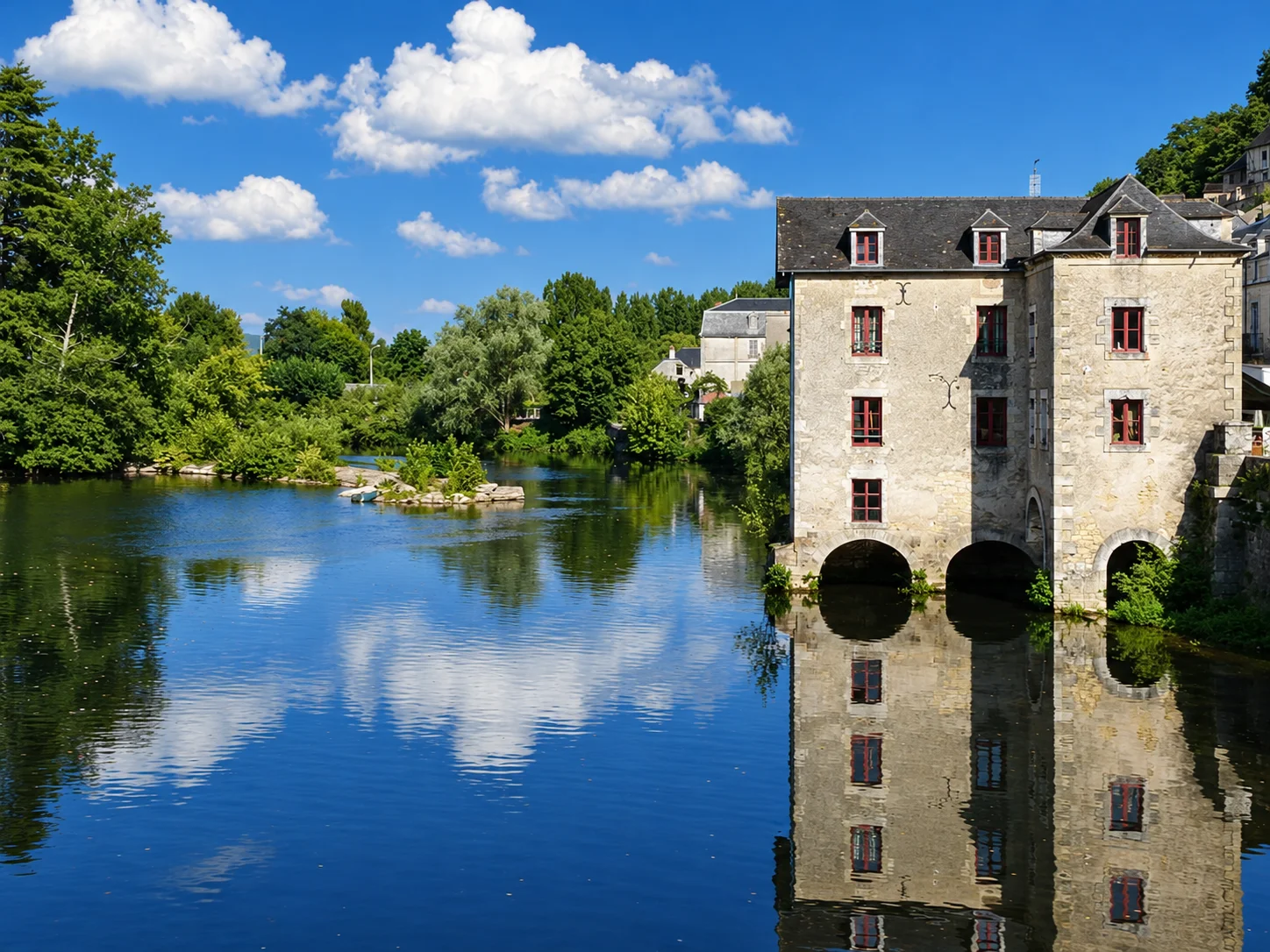 The old mill in Terrasson is reflected in the Vézère beside wooded riverbanks.
