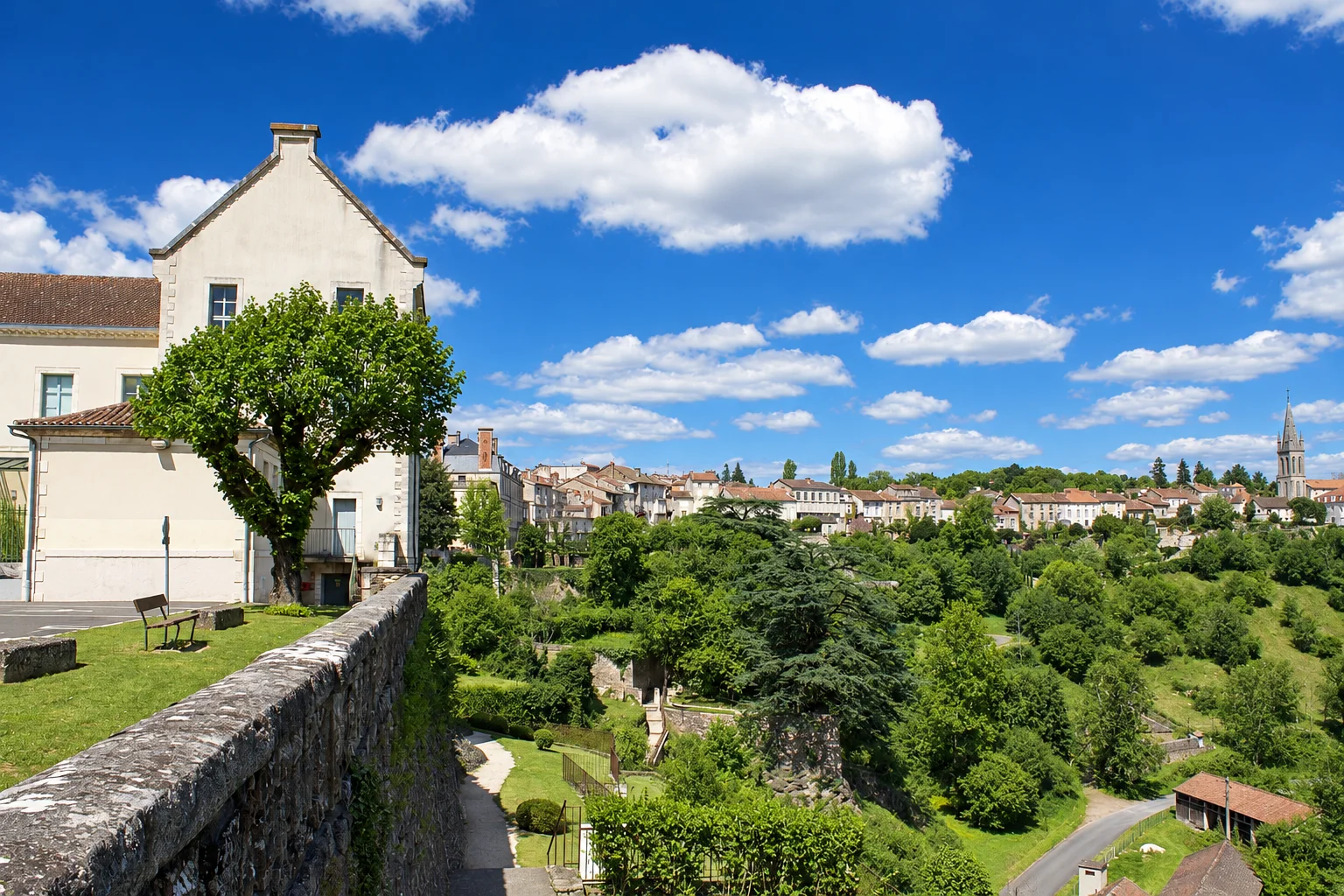 A stone parapet overlooks hillside gardens and the skyline of Nontron, with a church spire to the right.